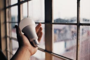 Hand holding a lightbulb by a window.